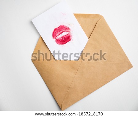 card with red lipstick kiss inside paper envelope on white background