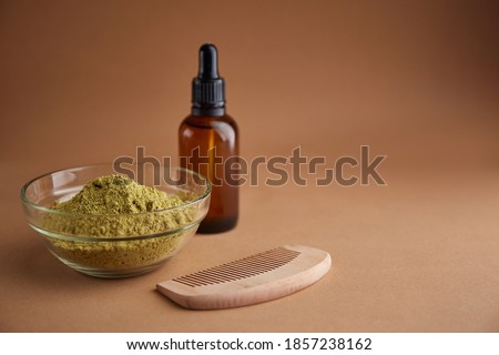 Henna mhendi colorant powder in a glass bowl and a wooden comb on a beige background top view. Ayurvedic hair care products. Natural care and hair coloring.
