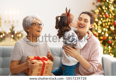 Merry Christmas and Happy Holidays! Cheerful kid presenting gifts to mom and granny. Parents and little child having fun near tree indoors. Loving family with presents in room.