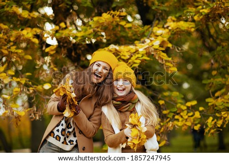Hello autumn. smiling modern mother and daughter in yellow hats with autumn yellow leaves outdoors on the city park in autumn.