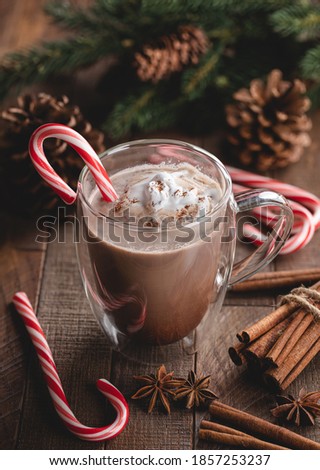 Glass cup of hot chocolate with candy cane and whipped cream on a rustic wooden table