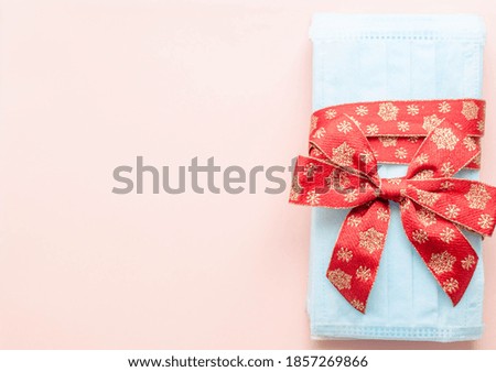medical protective face masks as a gift with a red ribbon on a pink background. Christmas and New Year 2021 decor. Holidays self-isolation and coronavirus pandemic concept