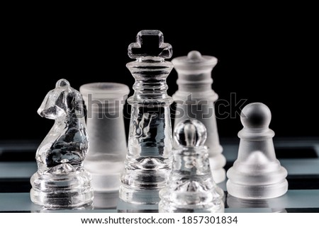 Glass chess pieces on a glass chessboard with reflection, on a black background.