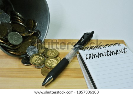 Commitment concept with coin, pen and noted book on table. 