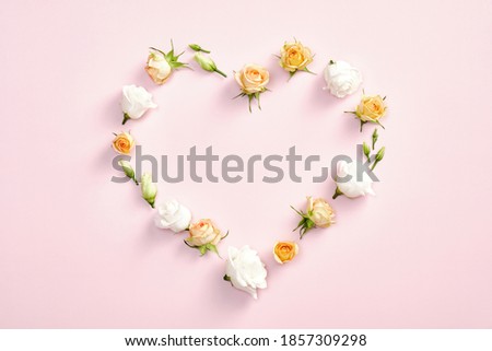 Heart symbol made of roses flowers and leaves on pastel pink background. Valentines day, mother day, anniversary celebration concept. Flat lay, top view.