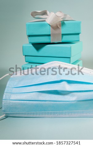 Stack of turquoise blue boxes, one tied with white silk ribbon and a face mask. Suitable for concepts like second or third wave of Covid-19 on xmas, Valentine's day or Mother's day