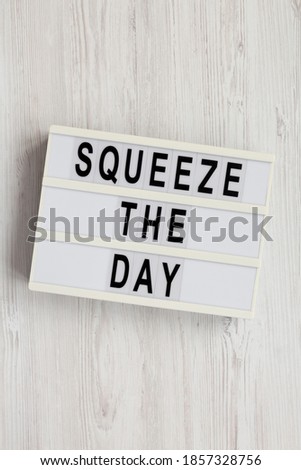 'Squeeze the day' on a lightbox on a white wooden background, overhead view. Flat lay, top view, from above. 
