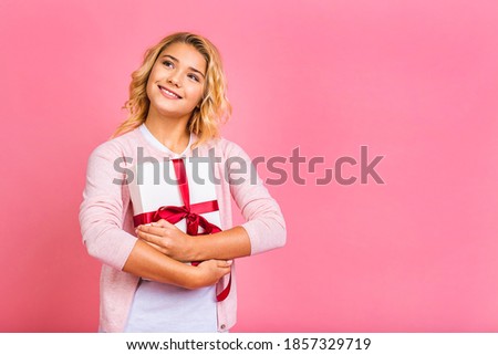Excited little kid girl 12-13 years old isolated on pink background with gift box. Childhood lifestyle concept. Mock up copy space. Pointing index finger on present box with gift ribbon.