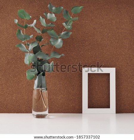 Wooden frame and vase with eucalyptus branches, cork background. Mock up, copy space. Folk