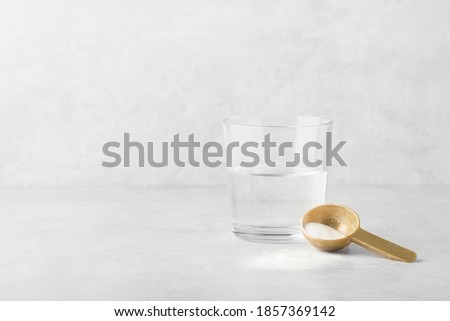 collagen powder with a glass of water on a gray background, spoon, beauty and youth Royalty-Free Stock Photo #1857369142