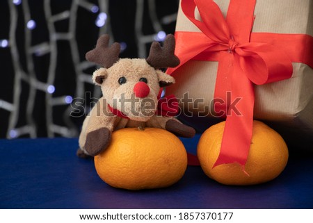 A gift wrapped in craft paper with a red wide ribbon stands on a blue table near the Christmas tree.