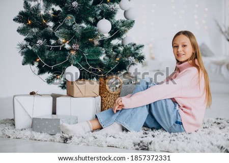 Little girl sitting by christmas tree