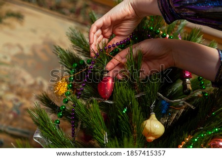 We decorate the Christmas tree. A hand hangs an original toy in the form of a red heart on a green branch of a Christmas tree


