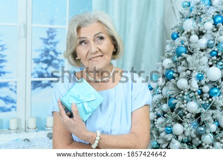 Portrait of happy smiling senior woman posing by Christmas tree