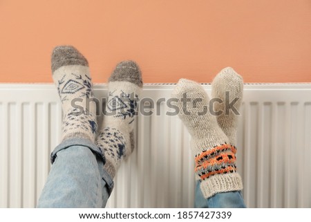 Couple warming legs on heating radiator near color wall, closeup