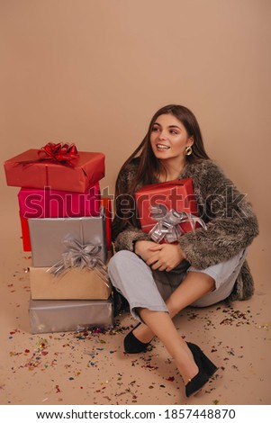 Smiling girl sitting near a pile of gift boxes  isolated over beige color background. 