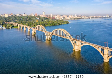 Merefo-Kherson arched railway bridge over the Dnieper river. View from above. Panorama of the city of Dnepropetrovsk. Dnipro city region. Sunny summer day. Aerial view. Royalty-Free Stock Photo #1857449950