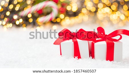 Christmas gift boxes with red ribbon and bow on the snow with blurred lights on the background.