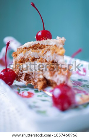 Peace of Honey cake with sour cream decorated with cocktail cherry is on a plate close-up.