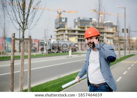 Young architect holding mobile phone and blueprint while looking away.