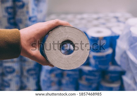 A shopper in a supermarket holds a roll of toilet paper