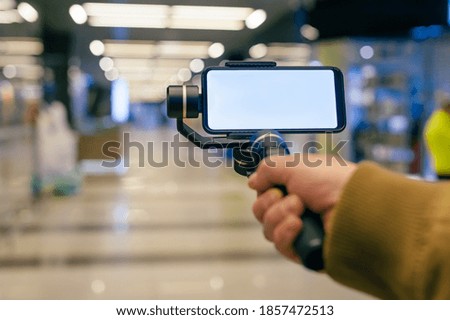 A man holds a smartphone with a stabilizer in his hand. Blogger in the mall