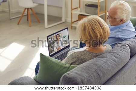 Using eHealth and telemedicine services at home. Couple of senior patients sitting on sofa with laptop, having video call with online doctor and getting professional health consultation Royalty-Free Stock Photo #1857484306