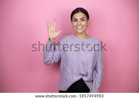 Beautiful woman wearing a casual violet sweater over pink background doing hand symbol