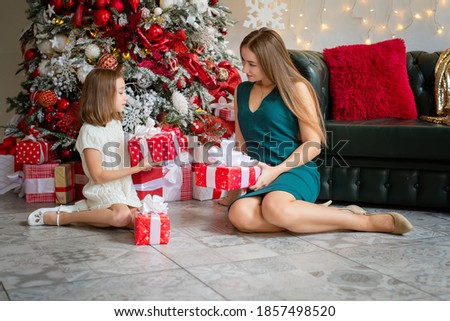 Two happy sisters aged eight and fifteen exchange gifts in a beautiful Christmas interior
