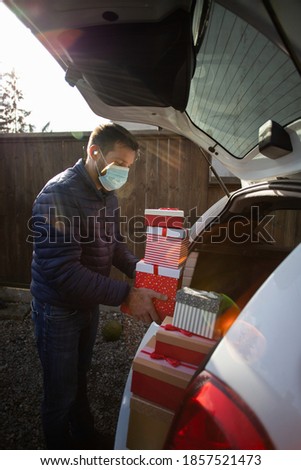 man with mask packing Christmas presents in car