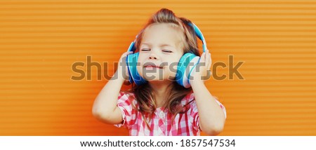 Portrait of little girl child in wireless headphones listening to music over orange background