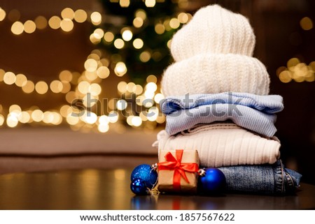 Winter holiday white sweater and hat, jeans with a gift with a red ribbon and blue balls on the background of a garland