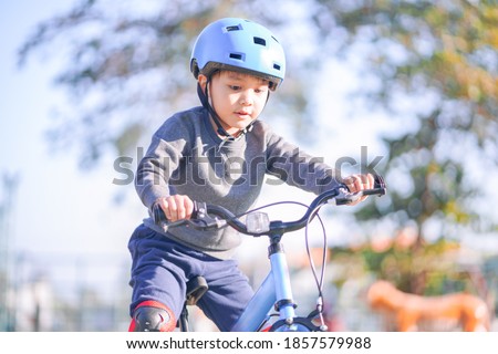 Portrait of cute small active asian boy wearing sport helmet riding small bicycle for kid alone in outdoor park during beautiful sunny days