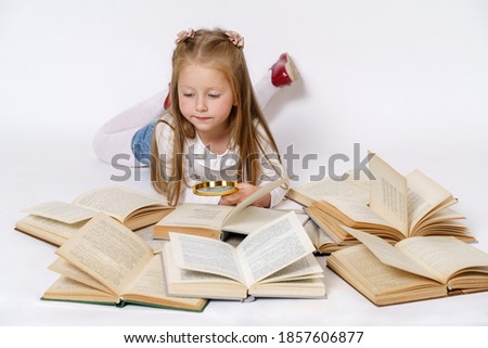 Education and people concept. The girl lies on the floor and reads books with a magnifying glass. Isolated over white background.