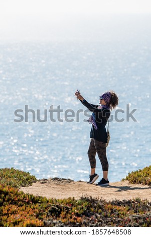 Woman taking selfie on rock with ocean in background. Bodega Bay Northern California
