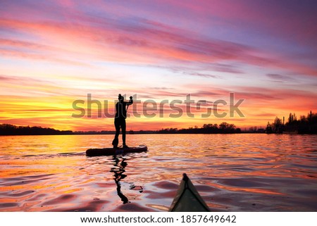 Silhouette of woman paddle on SUP (stand up paddle board) on quiet river at dusk. Winter sport