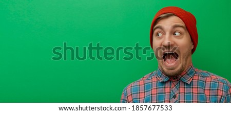 Close up portrait of attractive young model isolated on green background. Young man is surprised. 
Hipster