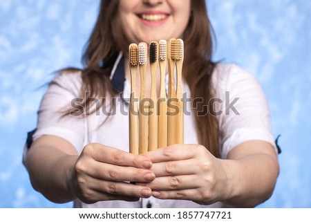 many bamboo toothbrushes in female hands close-up. girl with a defocused smile. environmentally friendly biodegradable hygiene items. multi-colored bristles. place for text. horizontal photo