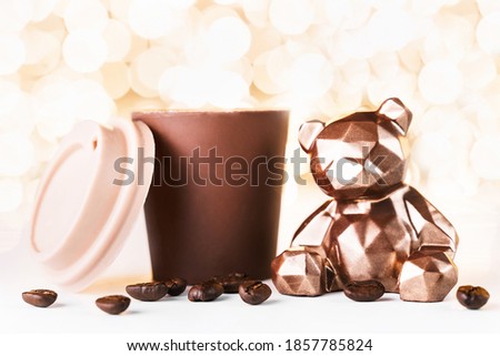 Gift card with chocolate bear and cup of coffee on golden background of christmas lights bokeh. Mockup for decorative design. Christmas and New Year concept. Copy space.