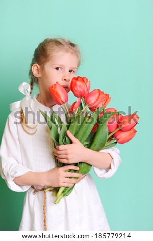 Little kid girl 10 year old smelling tulips. Wearing white stylish shirt. Holding flowers. 