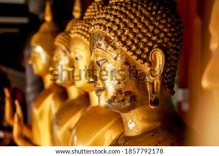 Closeup and crop old and golden face of golden Buddha statue on blurred golden Buddha statue stand strong line background