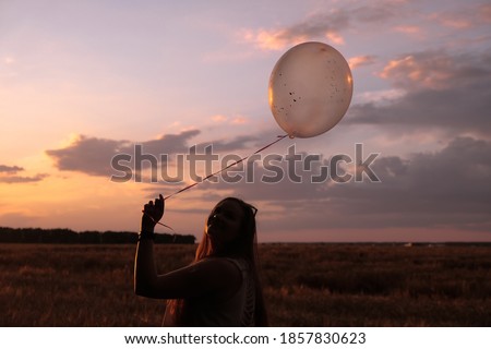Silhouette of female holding balloon with hearts against sundown purple sky.