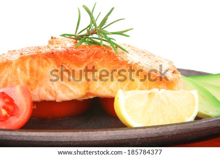 healthy sea food: grilled salmon on iron pan over wooden plate with lemon avocado and tomatoes isolated on white background