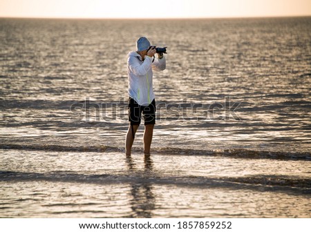 man films the sea at sunset

