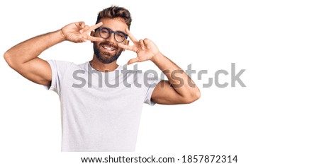 Young hispanic man wearing casual clothes and glasses doing peace symbol with fingers over face, smiling cheerful showing victory 