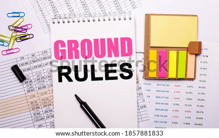 A notebook with text GROUND RULES, a marker, colored paper clips and bright note paper lies against the background of the graphs.