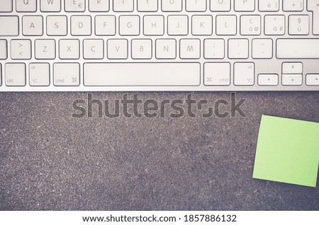 A top view of a computer keyboard and blank paper memo on a stone textured surface with copy space
