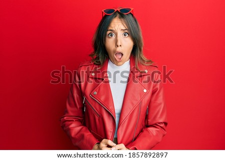 Young brunette woman wearing red leather jacket smiling making frame with hands and fingers with happy face. creativity and photography concept. 