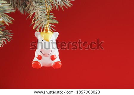 Ceramic Figure of a Unicorn on a spruce branch, on a red background. Free space for text.