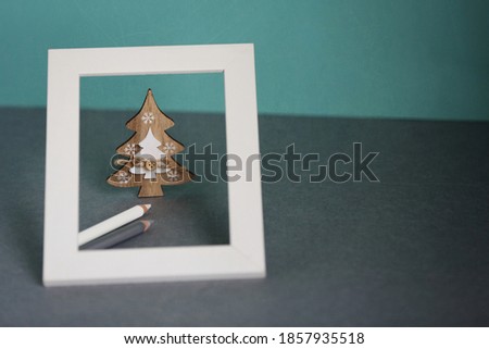 White wooden frame with Christmas tree toy inside and couple of pencils on blue background, copy space at right. Sustainable Christmas. Zero waste concept. Simple greeting card template